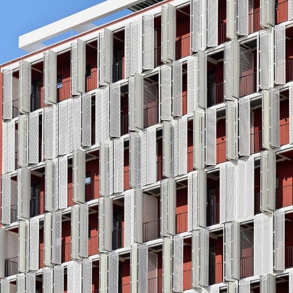 Many white expanded metal sunshades are installed outside the red exterior walls.