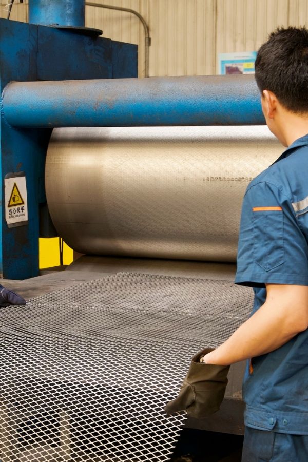 2 workers are feeding the expanded metal into the flattening machine.