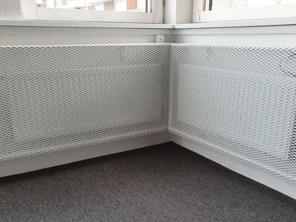 White expanded metal radiator cover is installed on the heating installation.