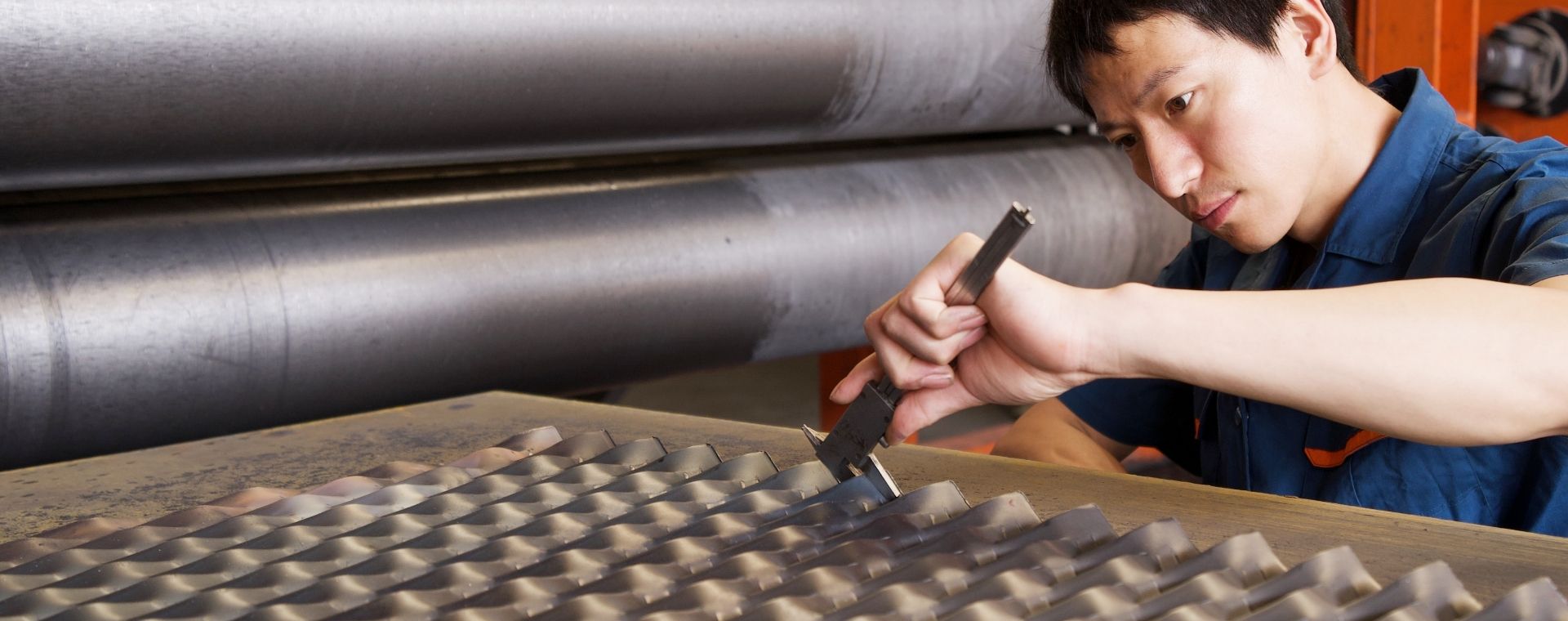 The worker is measuring the expanded metal size with a caliper.